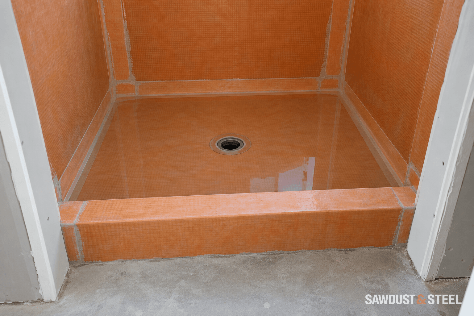 Shallow test water in an untiled shower pan with orange waterproofing membrane covering the walls and curb