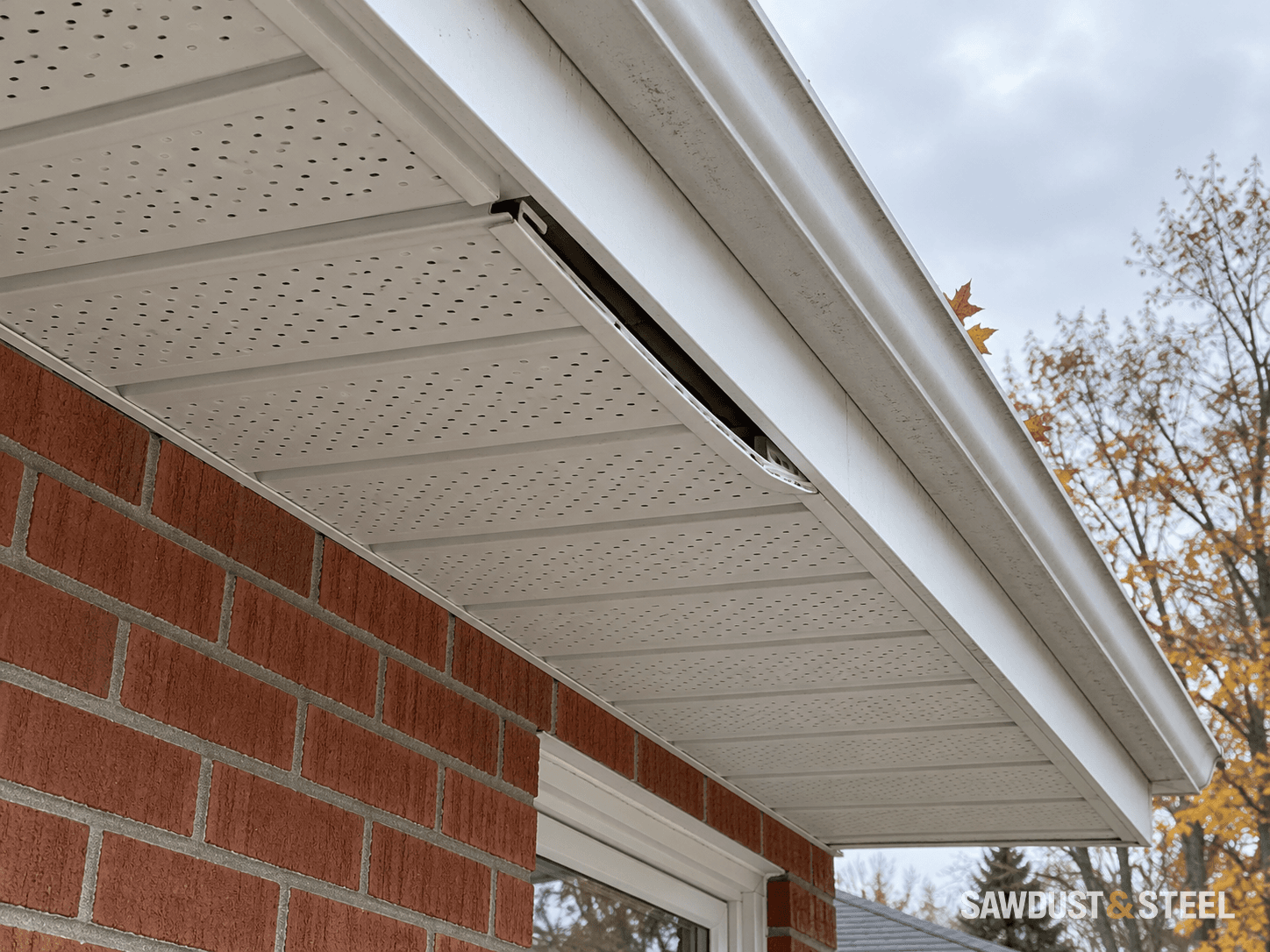 A white perforated soffit panel partly disengaged beneath a house gutter