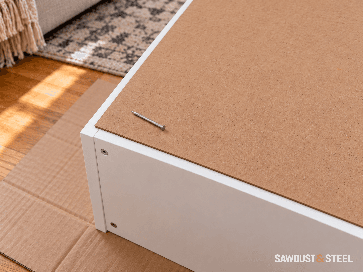 A thin hardboard cabinet back overlapping the white supporting rim, with a loose nail resting beside the corner