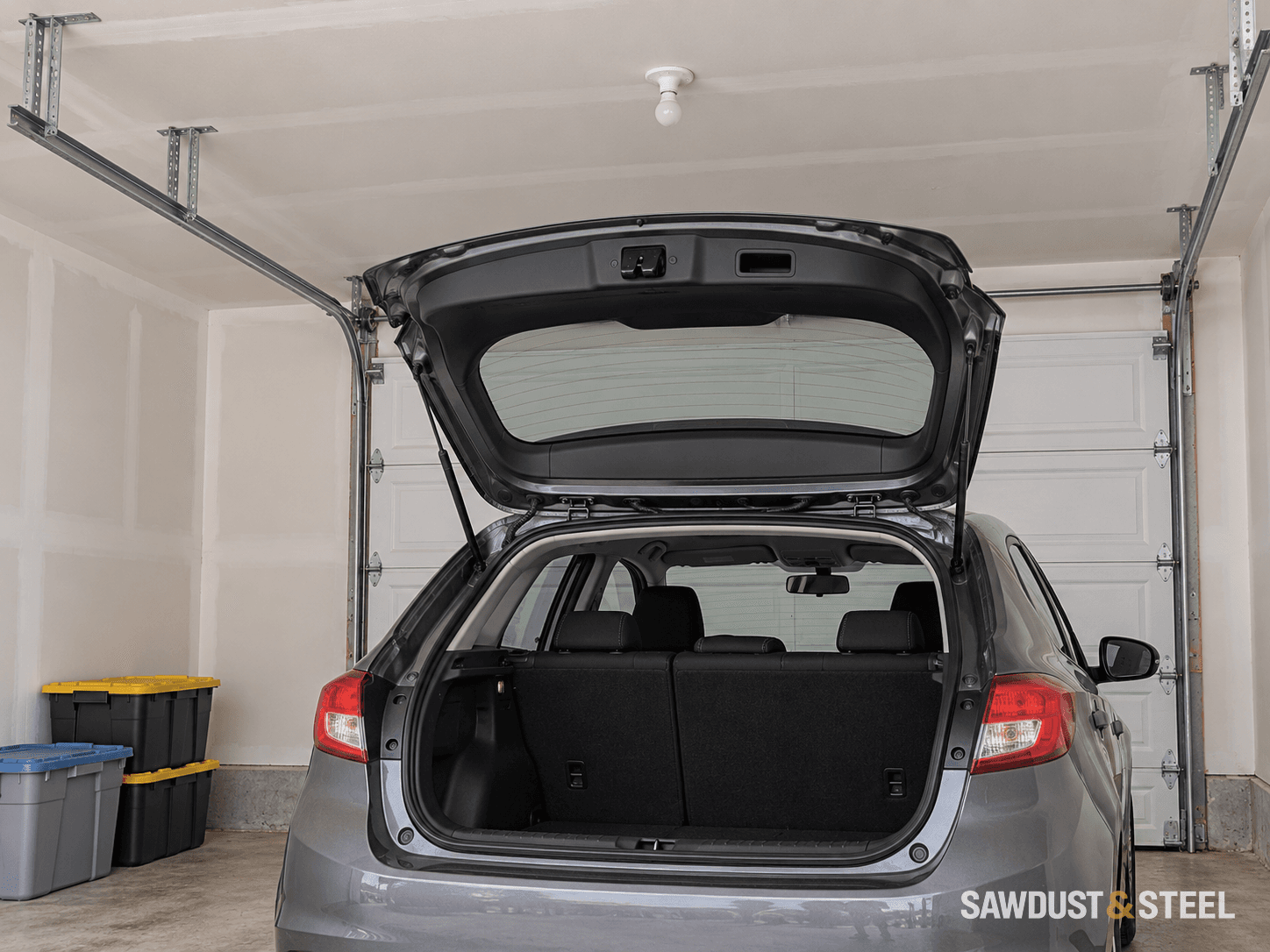 A parked hatchback with its tailgate raised beneath a garage ceiling and overhead door tracks