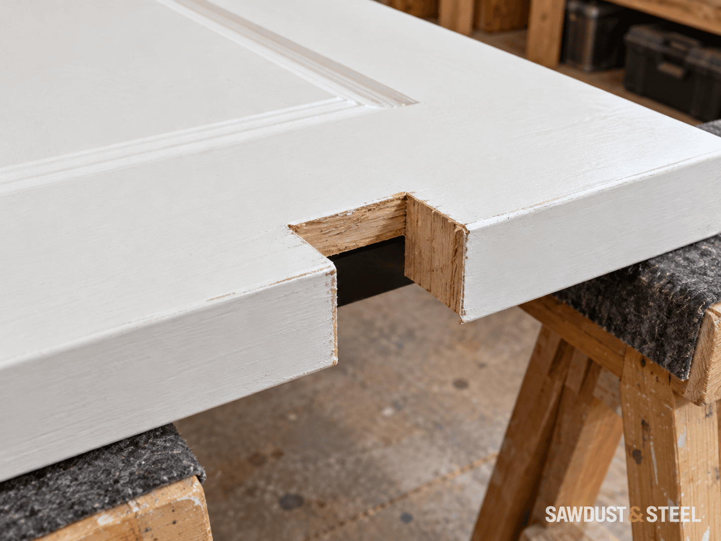 A rectangular hardware notch through the edge of a white door resting on padded trestles