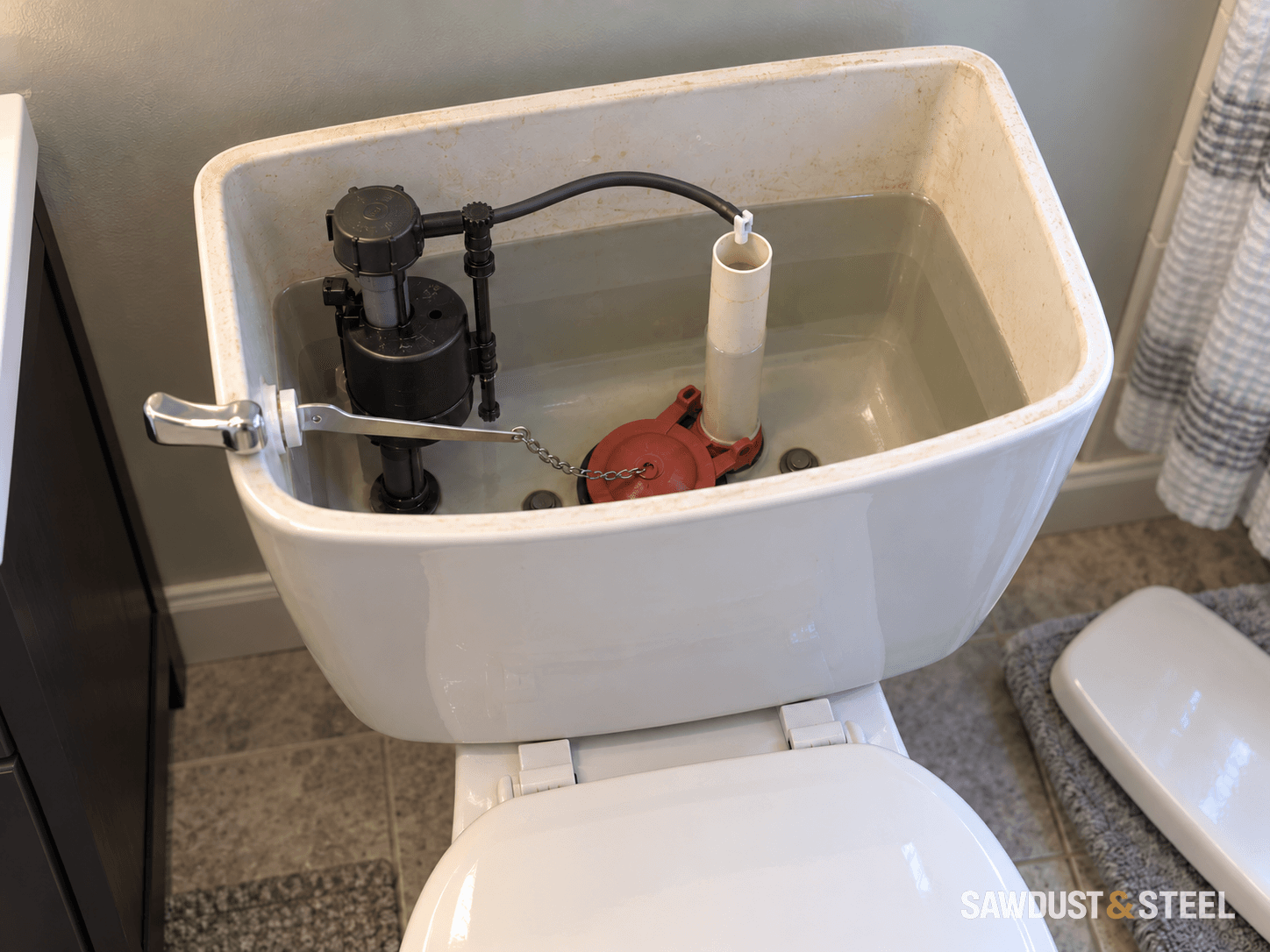 Open toilet tank with a fill valve, refill hose, overflow tube, flapper and chain