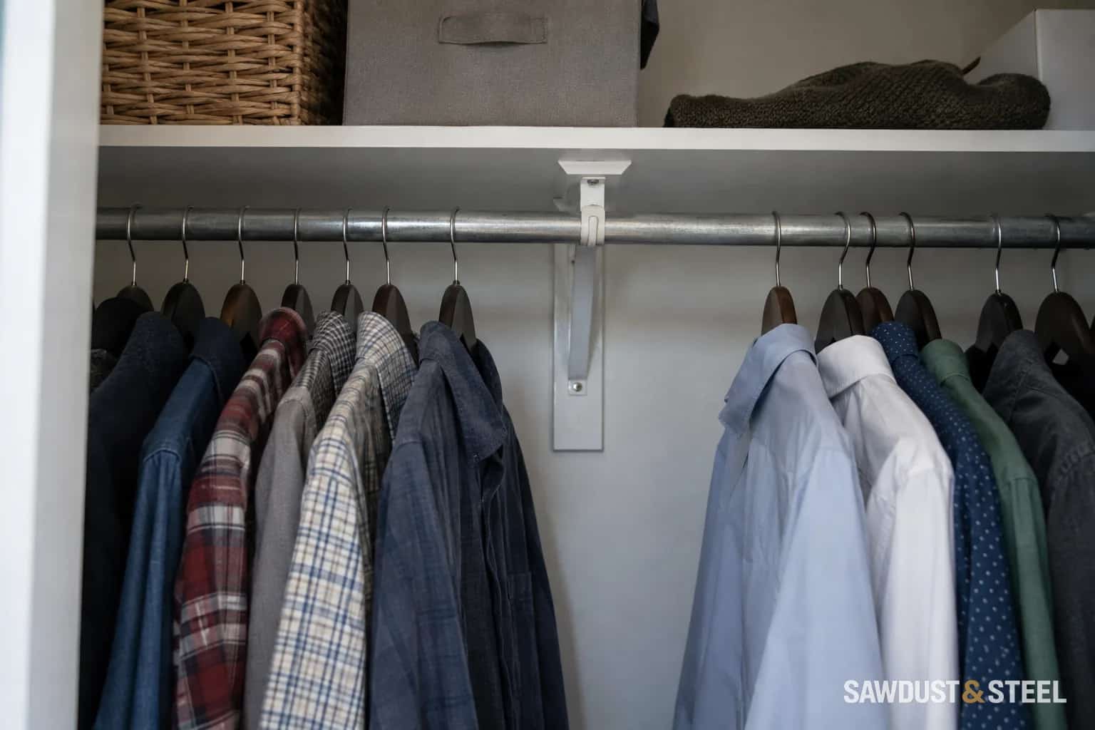 Shirts hanging from a metal closet rod with a centre support below a shelf.