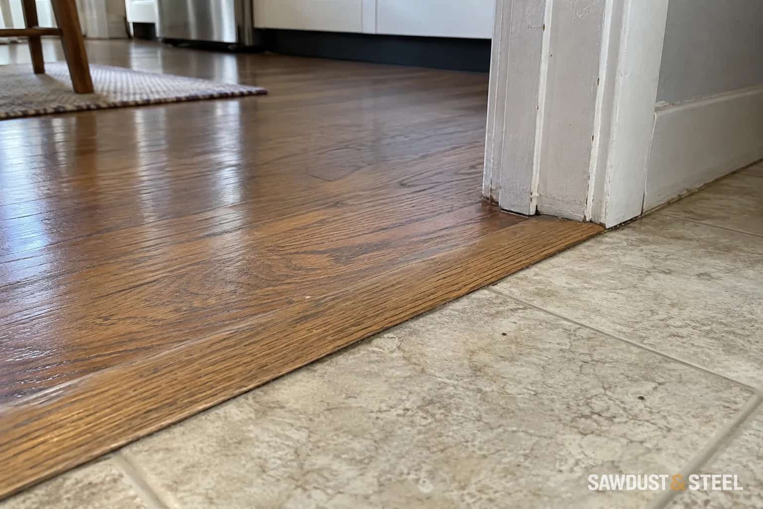 Oak reducer joining a wood floor to a lower tile-pattern floor in a doorway