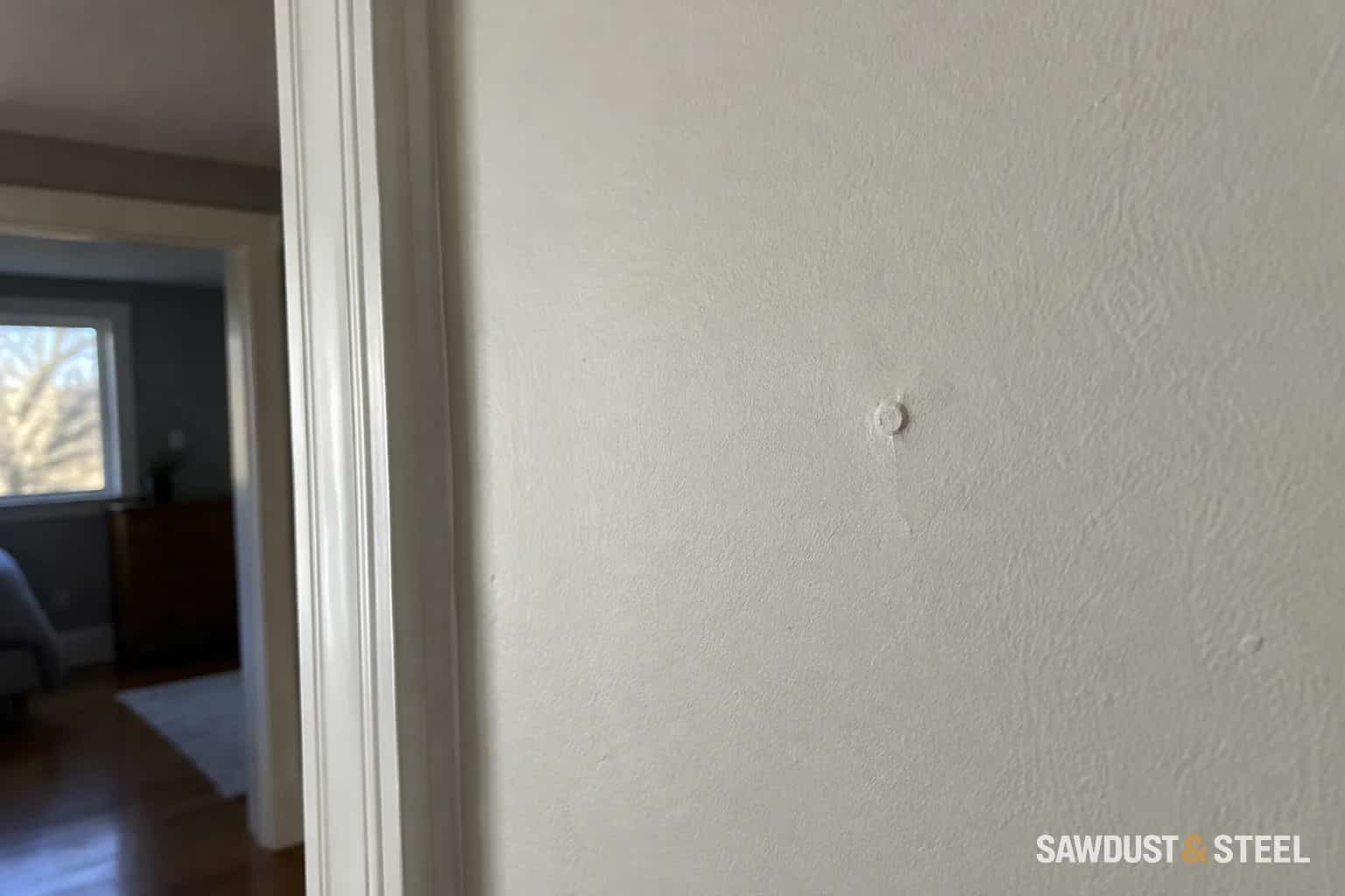 Small circular fastener pop visible beneath painted wall finish