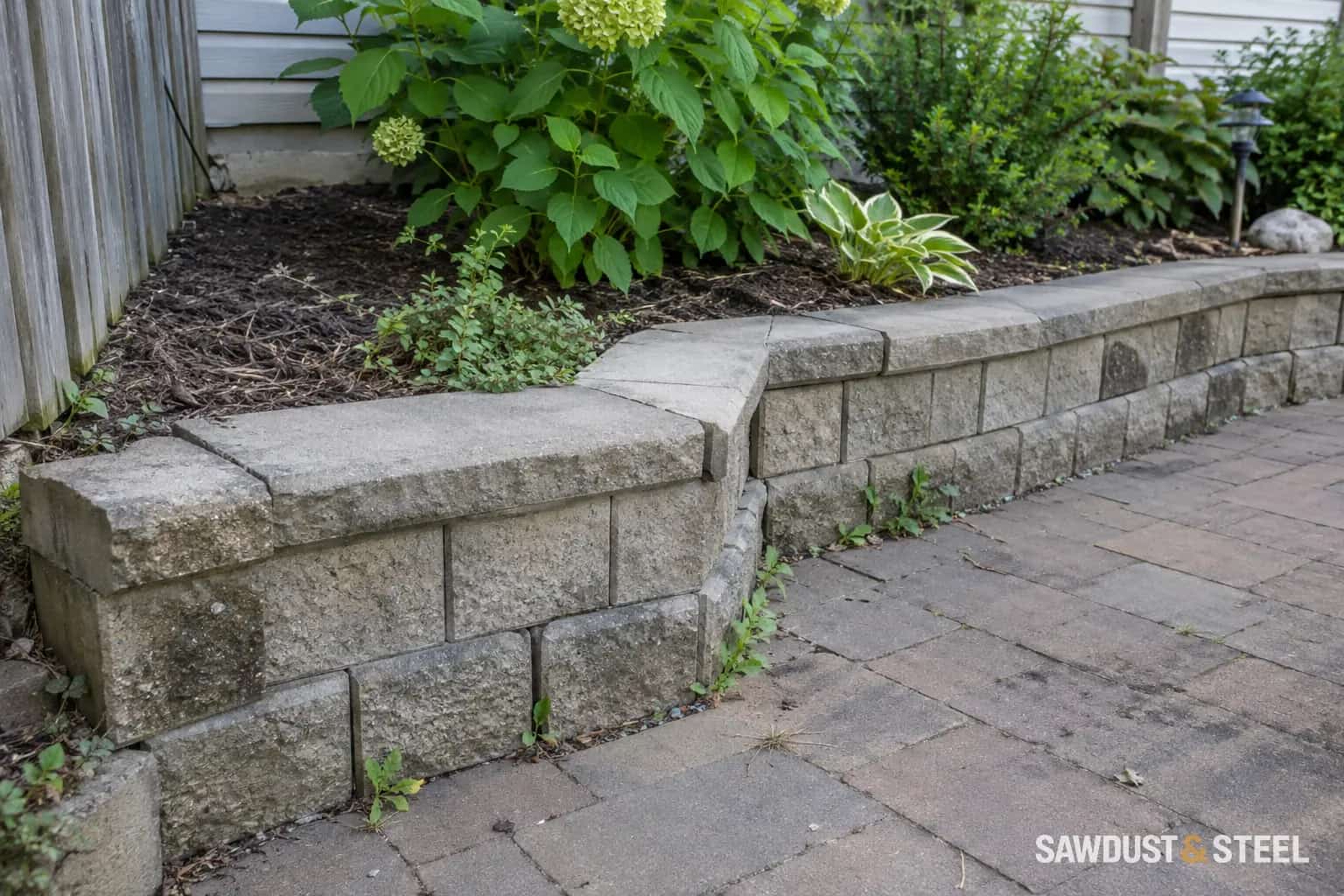 Low concrete-block garden retaining wall beside paving and a planted bed
