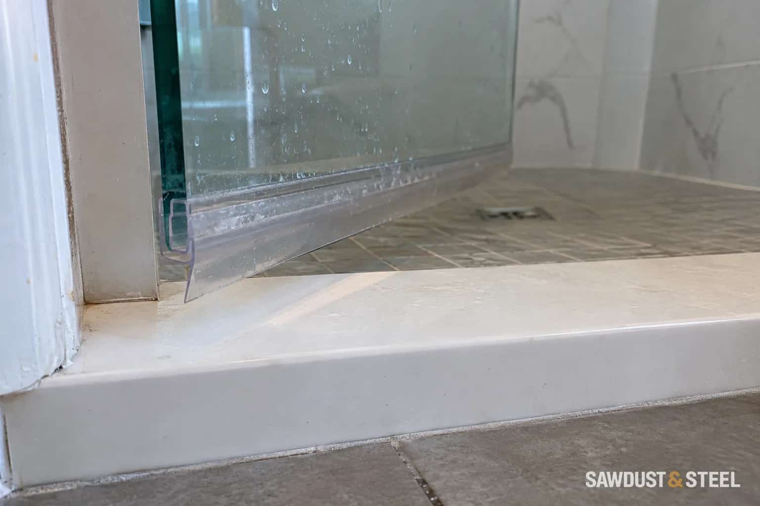 Clear sweep along the bottom edge of a glass shower door above a white curb
