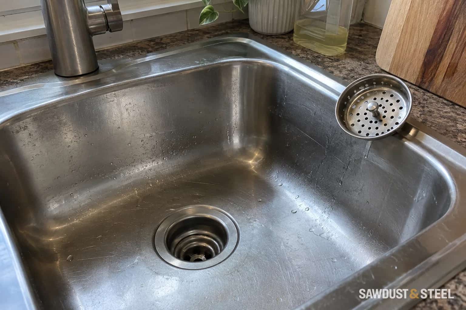 Removable basket strainer beside a stainless kitchen sink drain