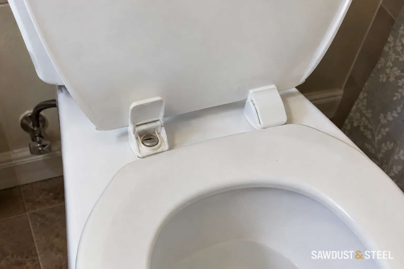 White toilet seat with one hinge cover lifted to show the mounting screw