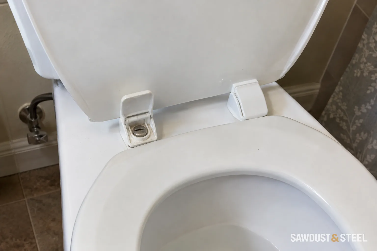Toilet lid raised above the seat with rear hinge fixing points visible