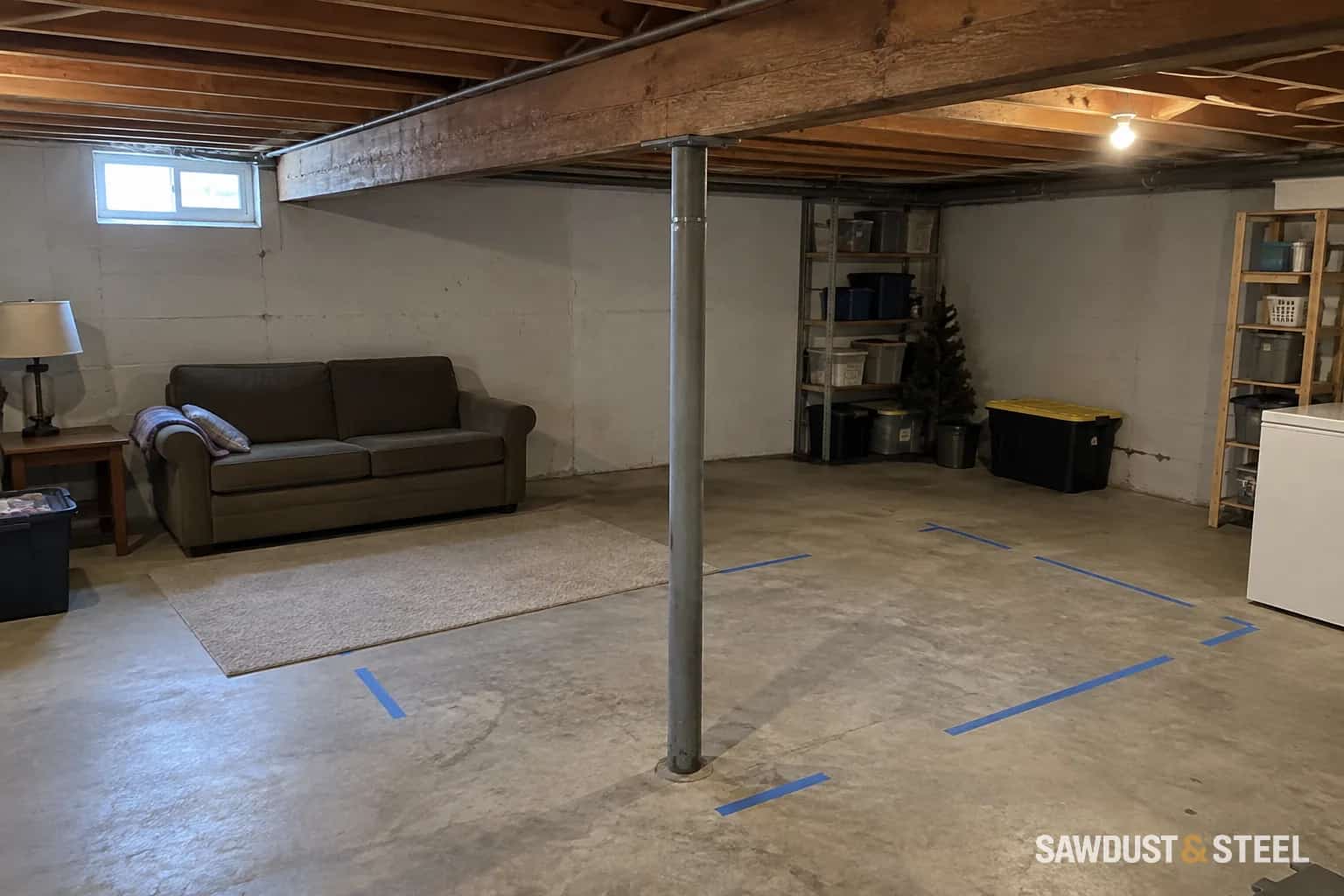 Steel support column beneath a basement beam beside a taped furniture layout
