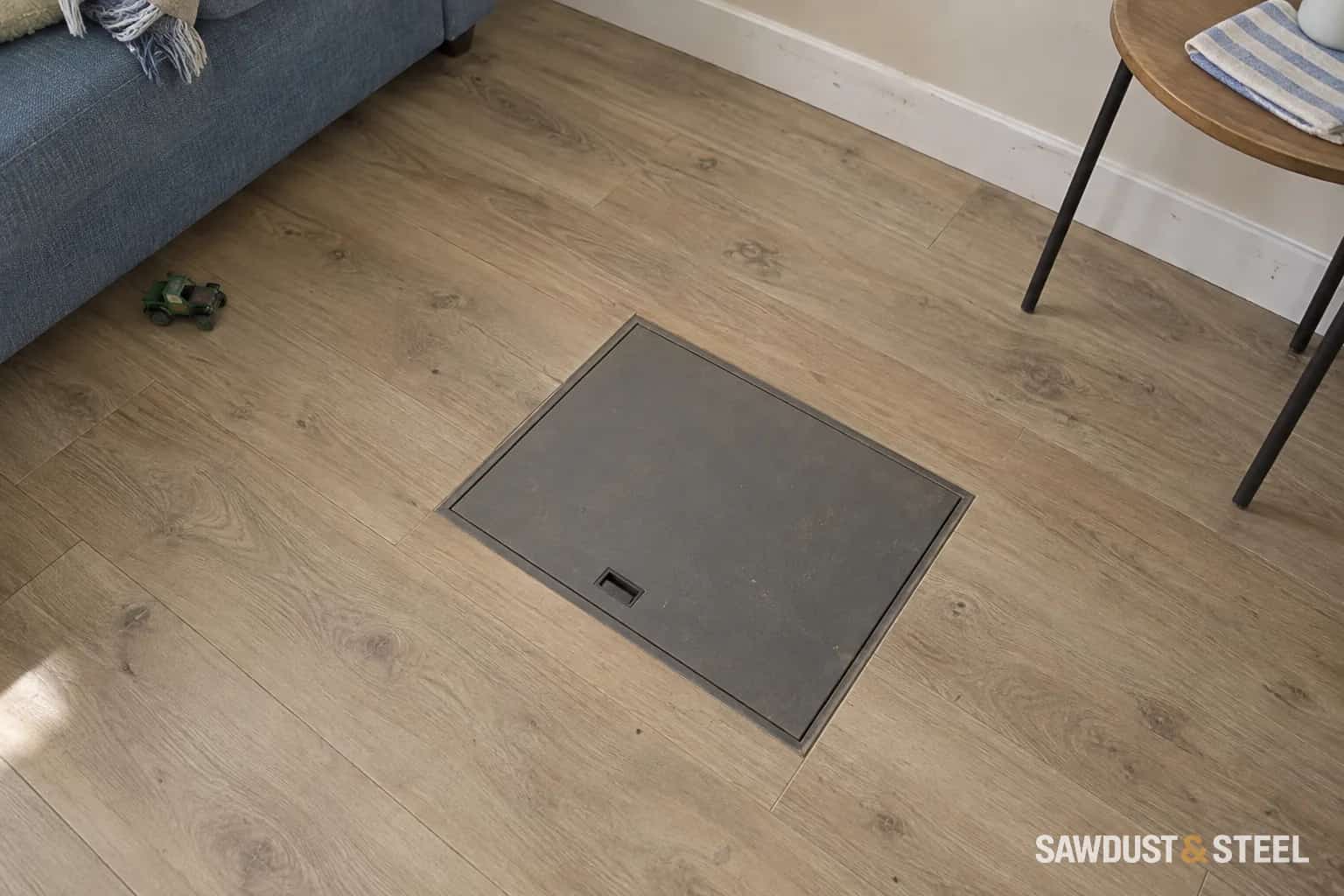 Flush floor access hatch with clear space between a sofa and movable side table