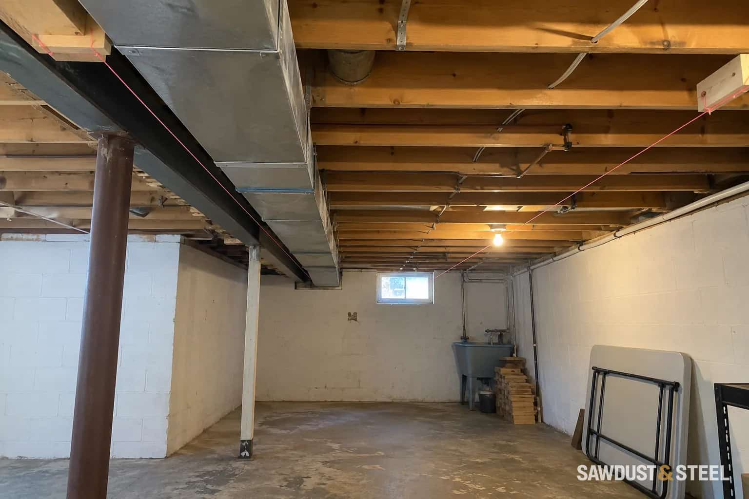 Exposed basement joists and ductwork with pink strings marking a proposed ceiling height