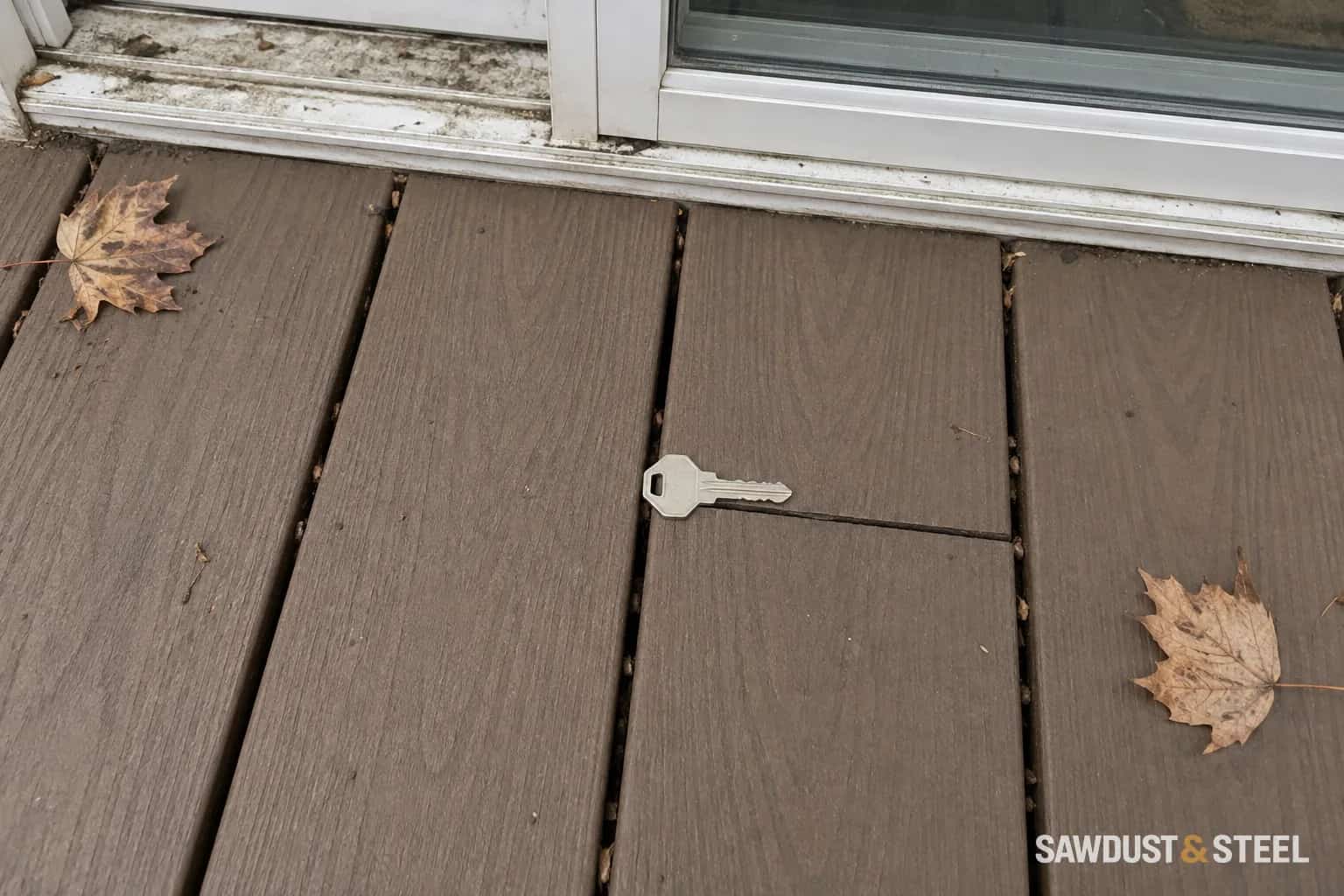 House key beside an open composite board joint near a weathered patio-door threshold