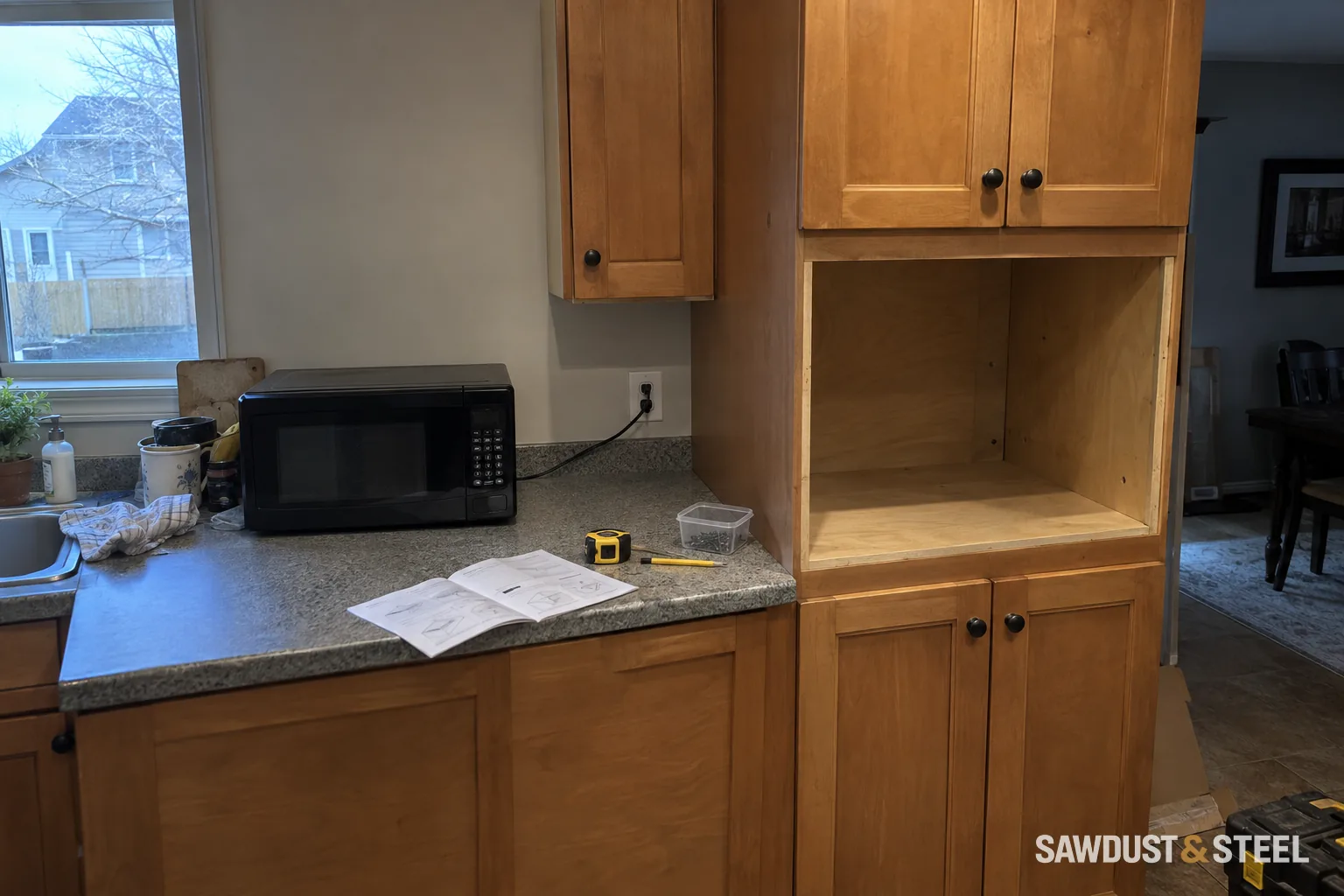 Black microwave on the countertop beside an empty unfinished wood cabinet niche