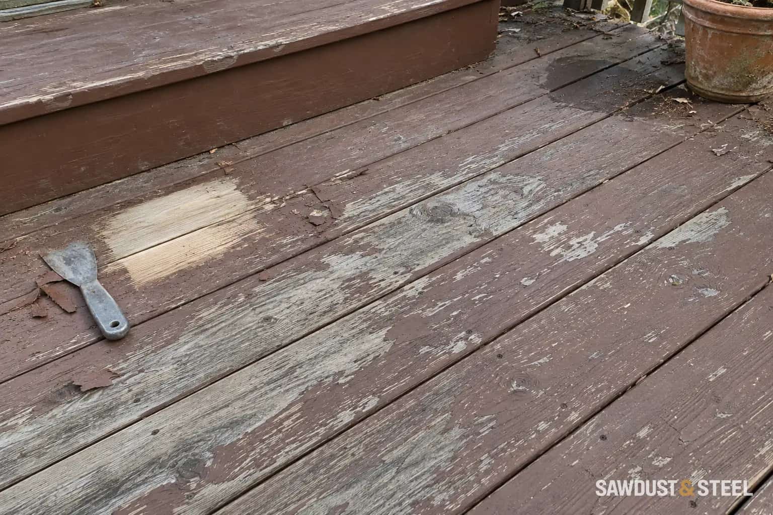 Peeling brown deck stain and a small stripped test patch beside a worn step and planter