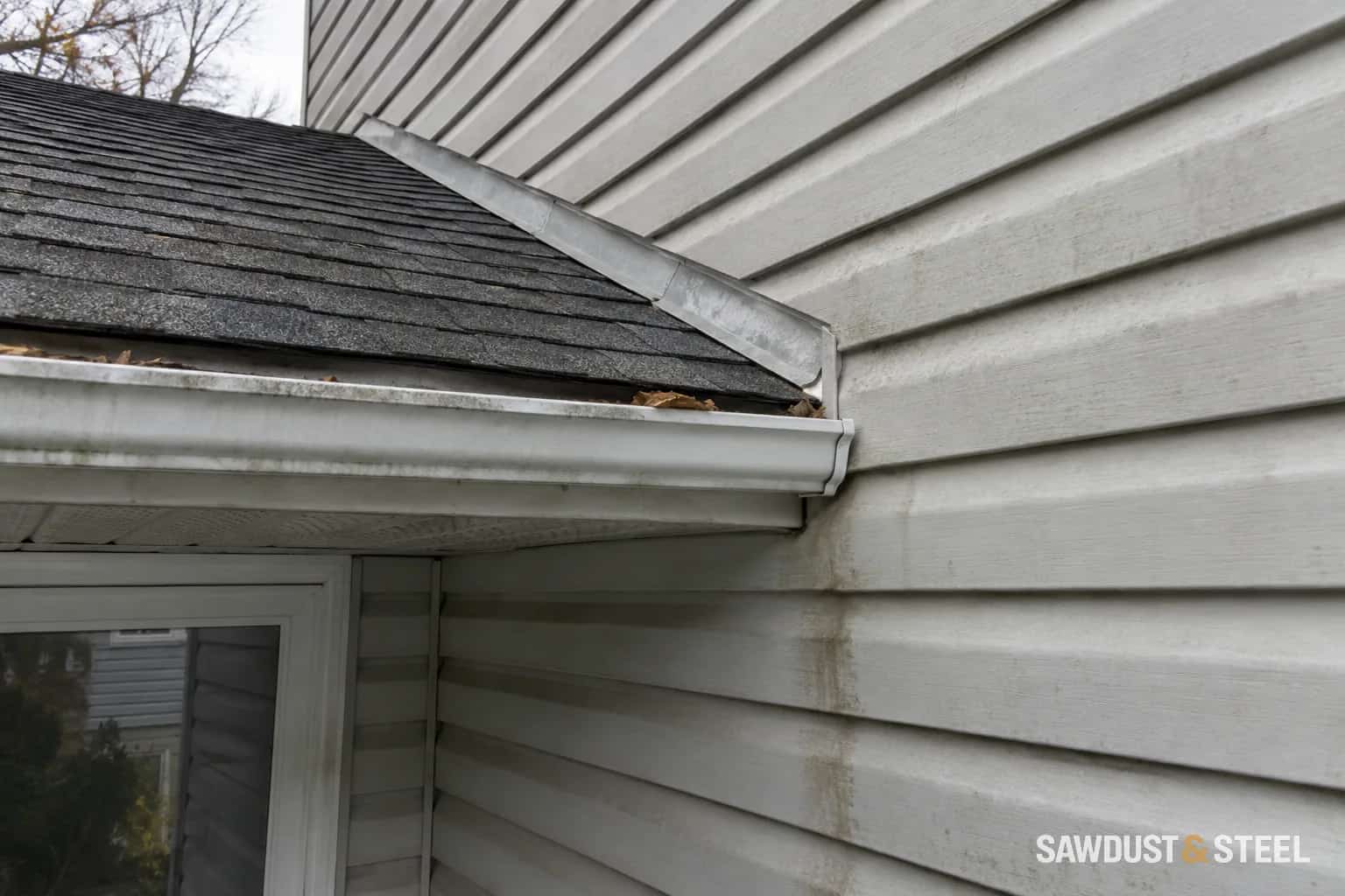 Water staining on pale siding below a porch roof and gutter end