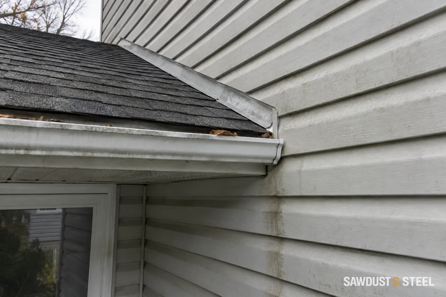 Water staining on pale siding below a porch roof and gutter end