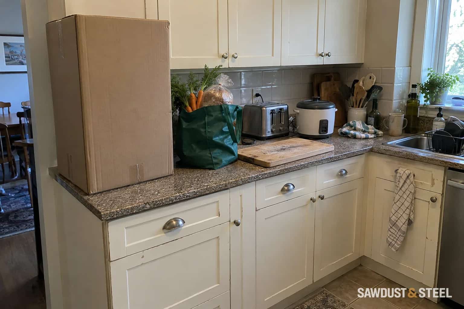 Cardboard pantry mock-up beside groceries, a chopping board and small appliances on a worn kitchen counter