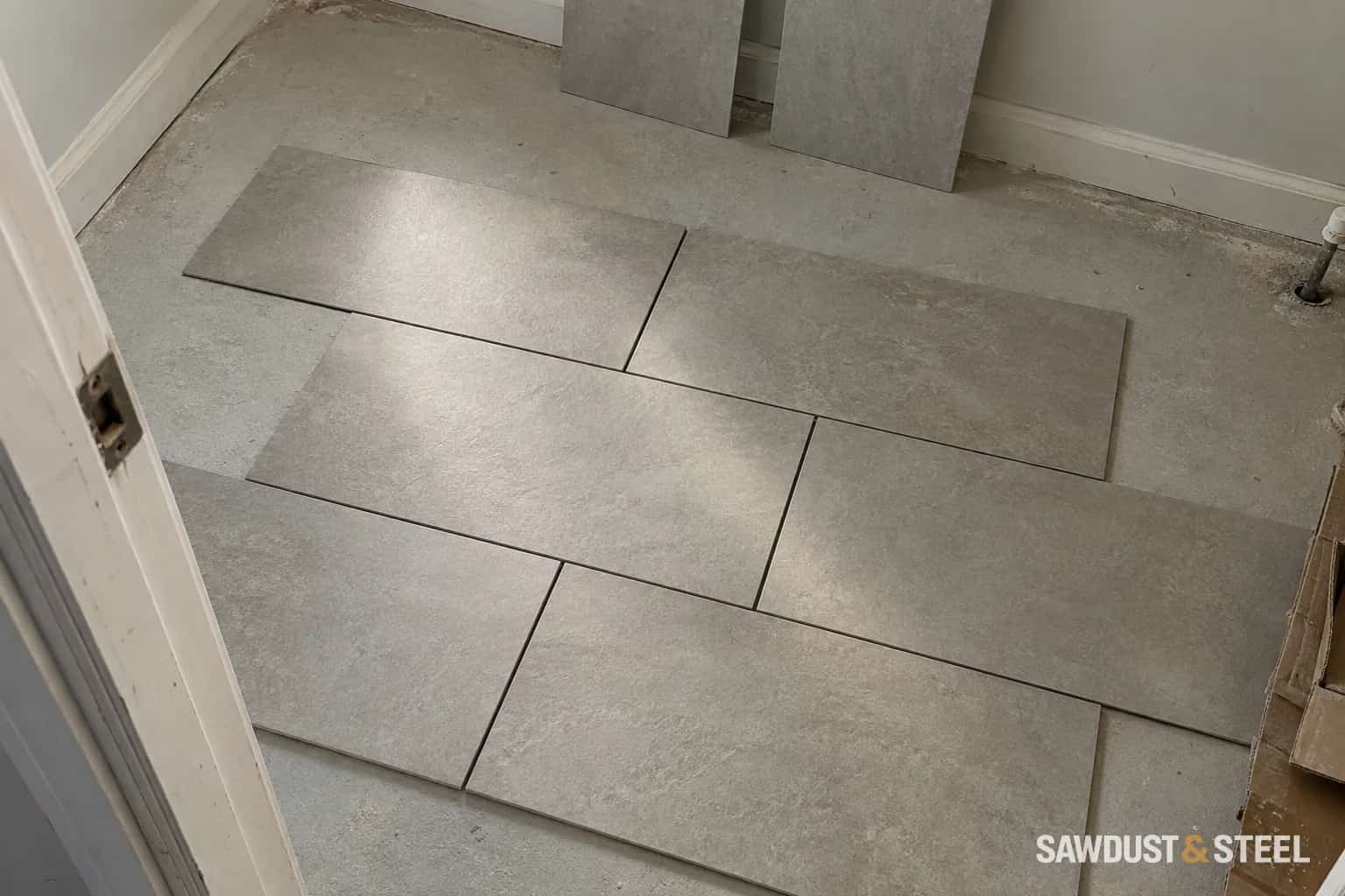 Grey rectangular tiles dry-laid in a staggered pattern on a dusty bathroom floor