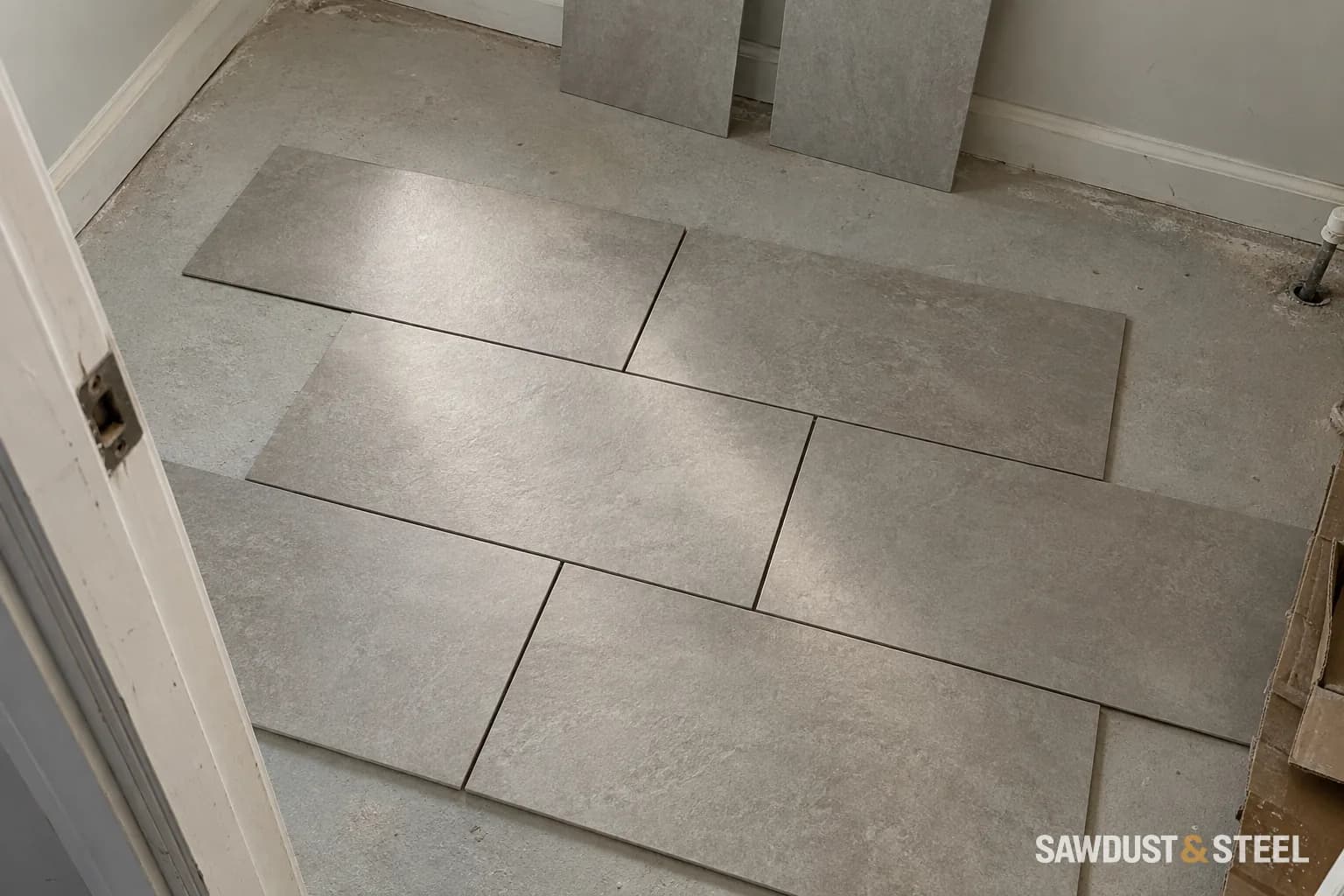 Grey rectangular tiles dry-laid in a staggered pattern on a dusty bathroom floor