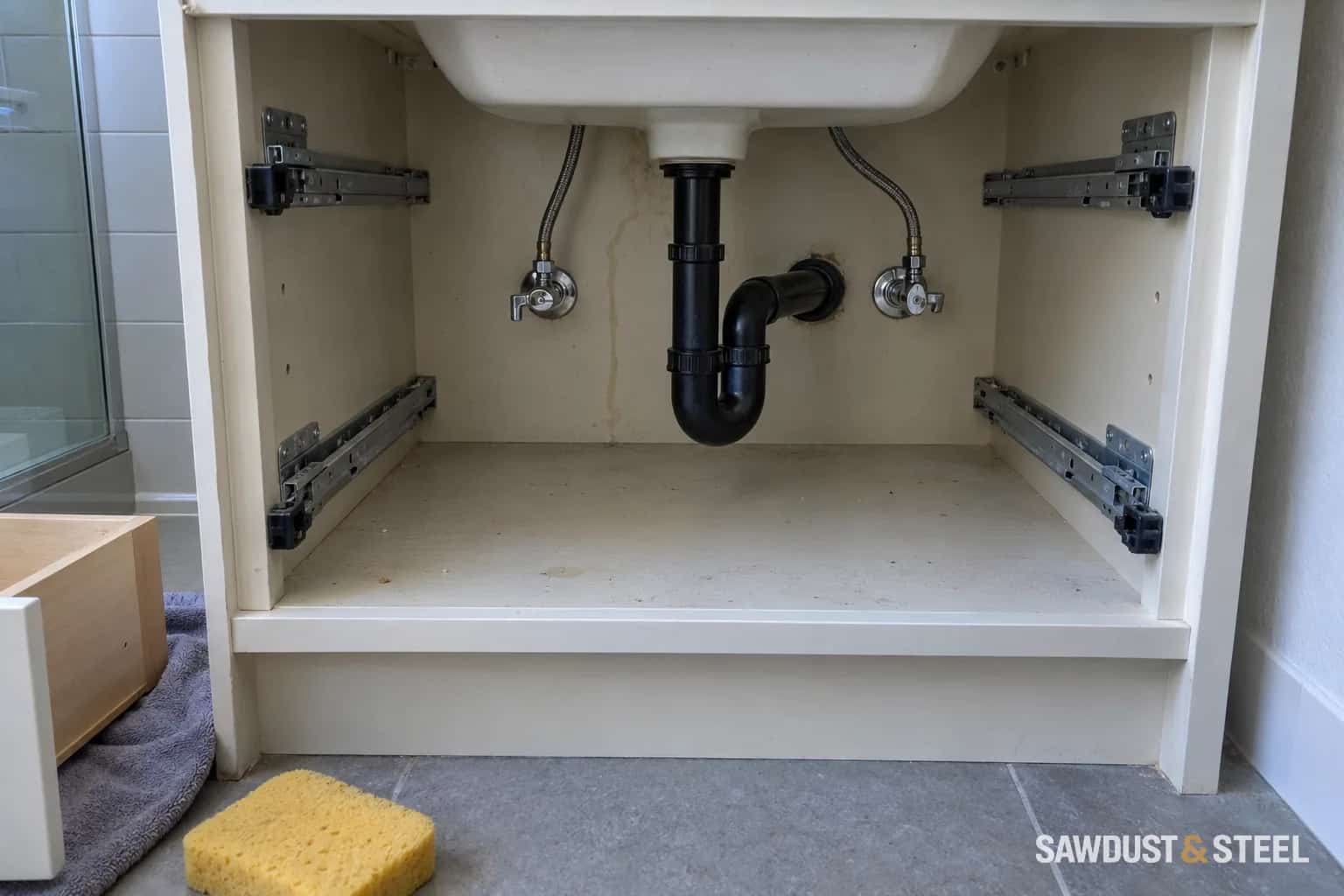 Bathroom vanity with drawers removed, showing the black drain trap, shutoff valves, and side-mounted drawer runners