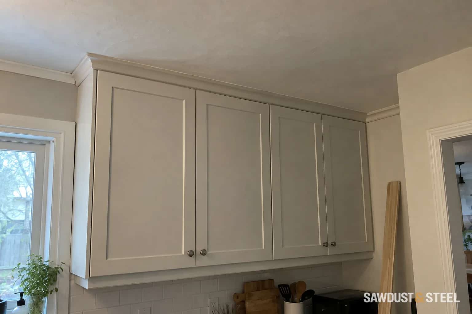 Simple crown trim and a narrow filler above painted kitchen cabinets beneath an older plaster ceiling