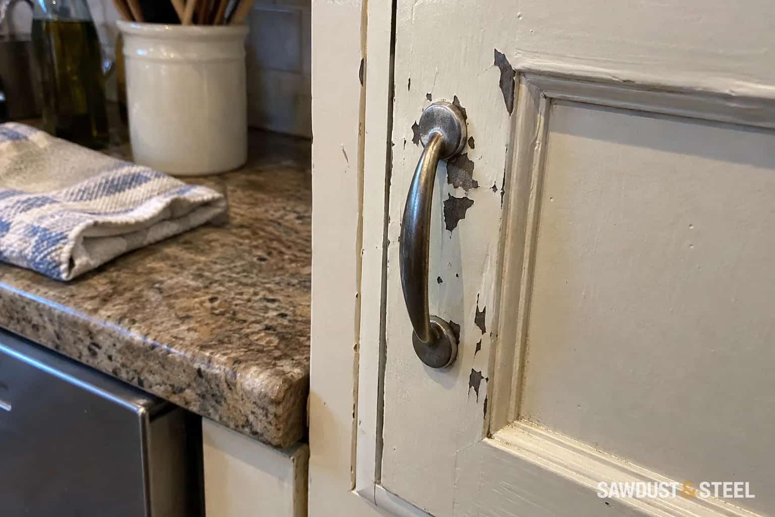 Peeling paint around the handle of a kitchen cabinet door.