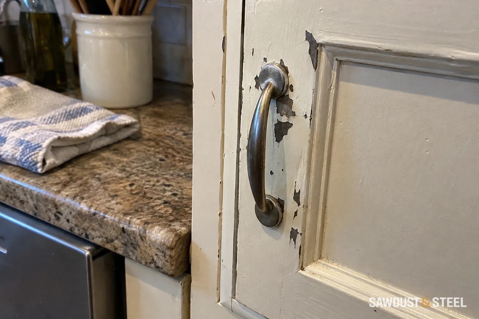 Peeling paint around the handle of a kitchen cabinet door.
