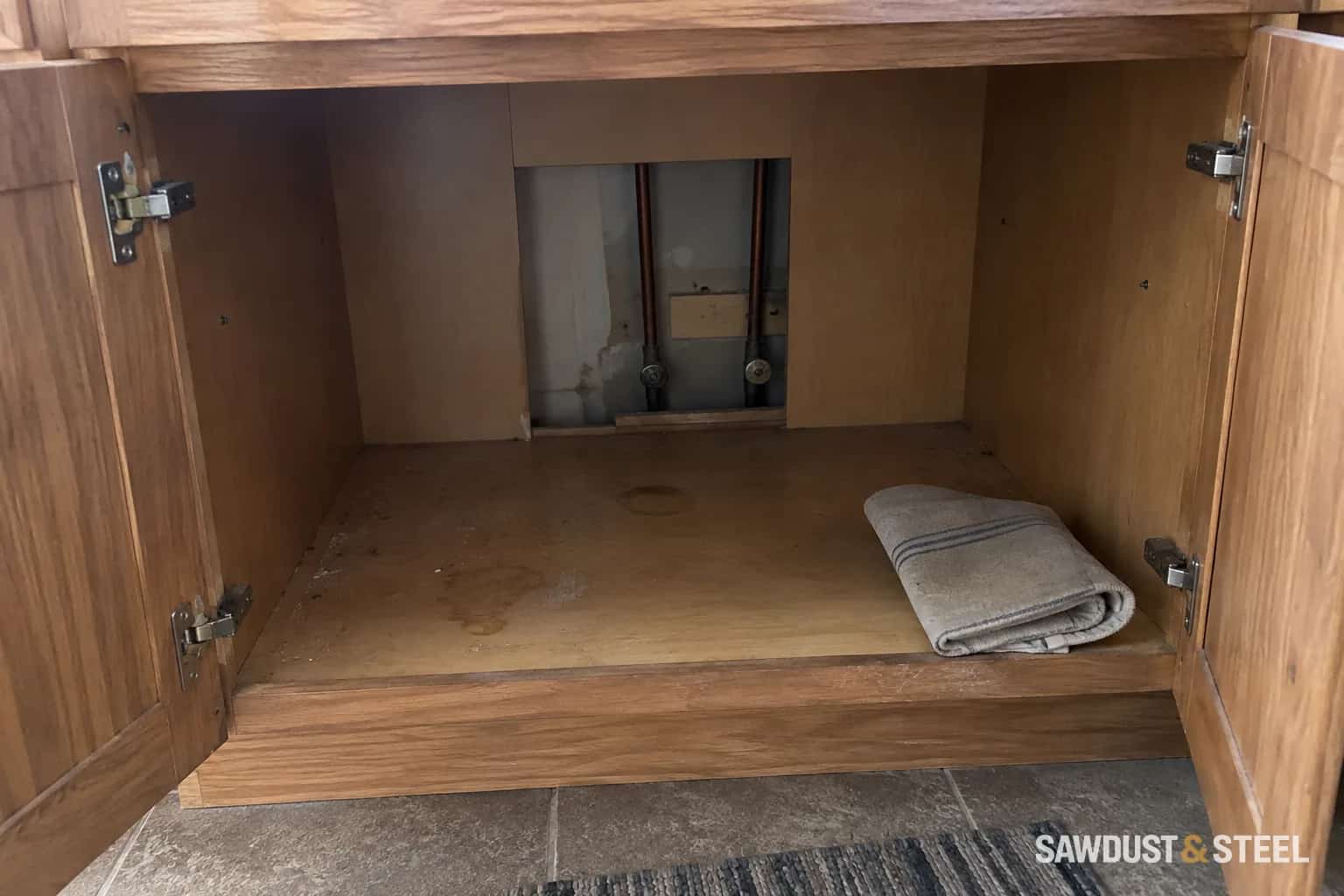 Open timber sink cabinet with rear openings around copper supply pipes and valves