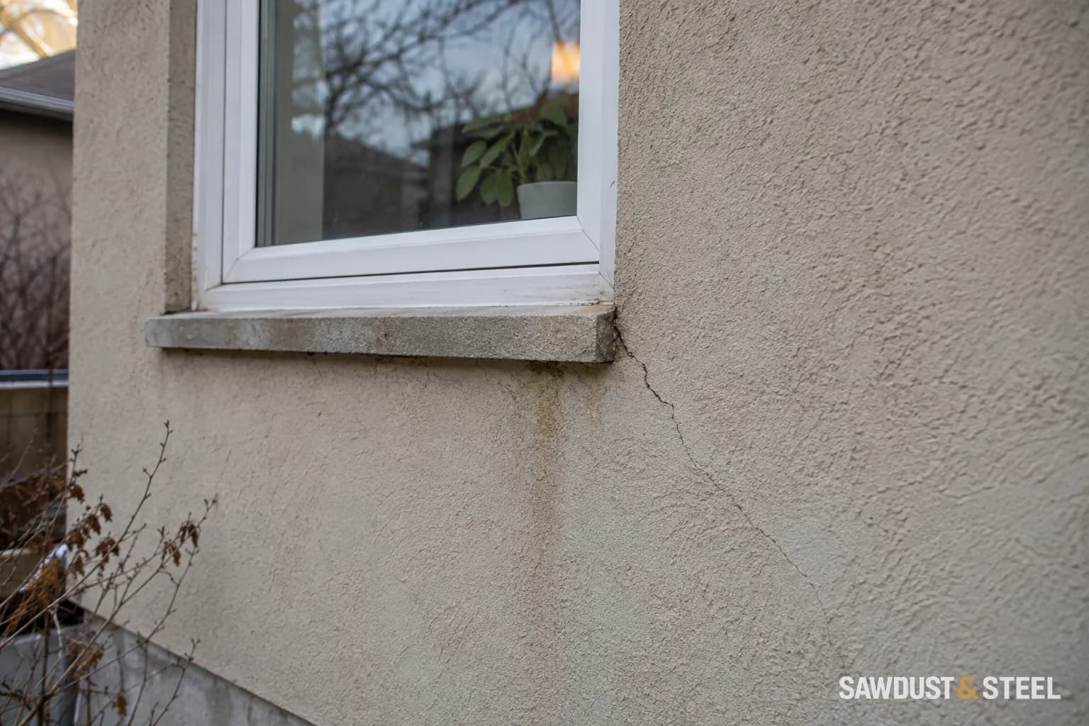 Fine crack and a faint water stain below a window in a stucco wall.
