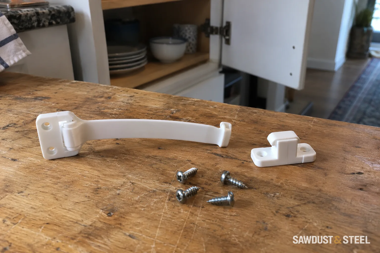 Uninstalled white cabinet safety latch, separate catch and four screws on a wooden workbench