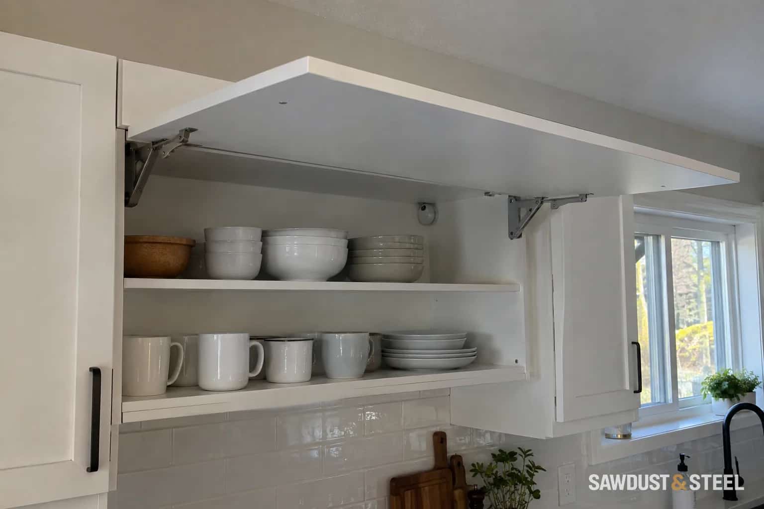Upward-opening wall-cabinet front raised above shelves of cups and bowls