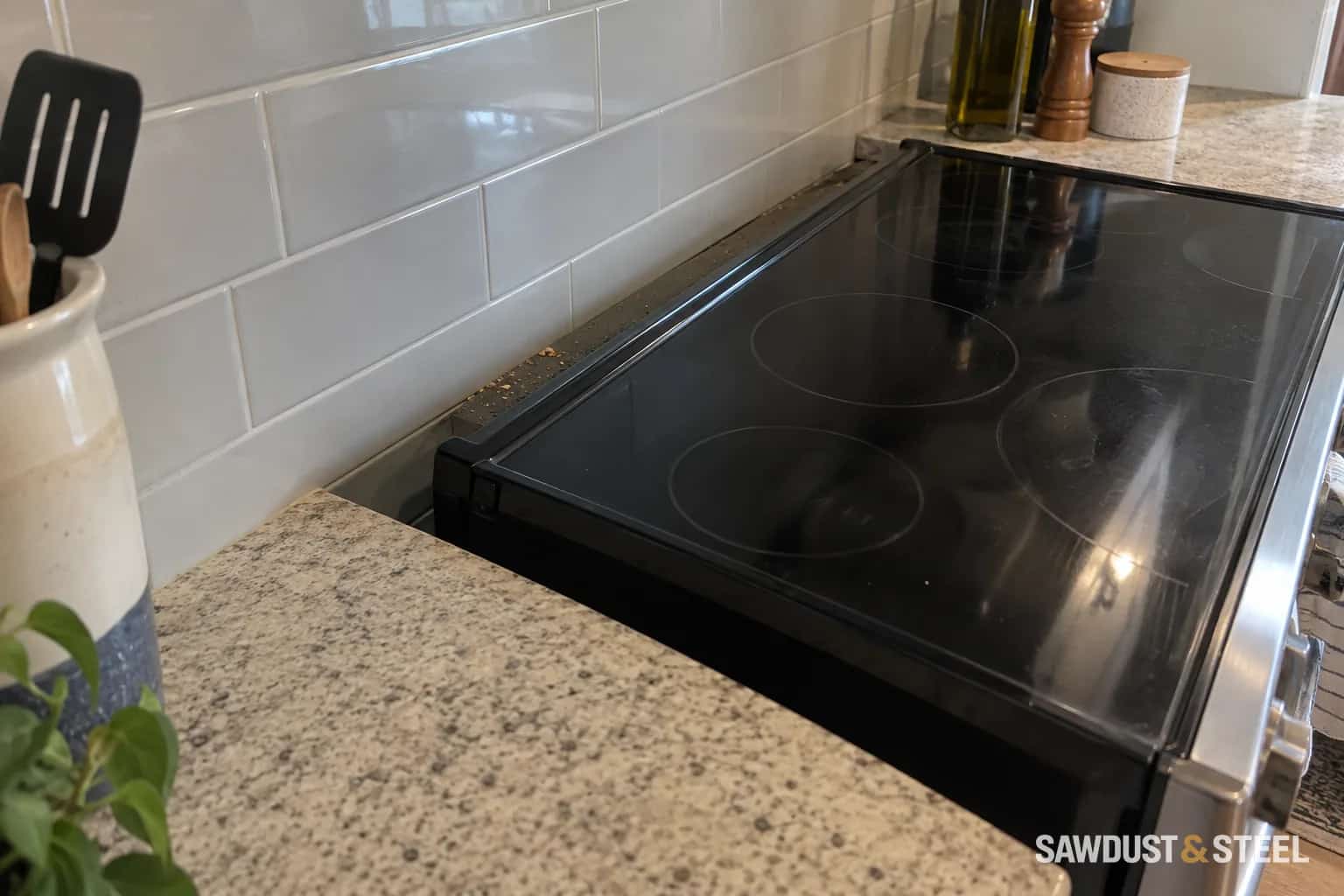 The rear edge of a black glass slide-in electric range with a gap beside the tiled backsplash